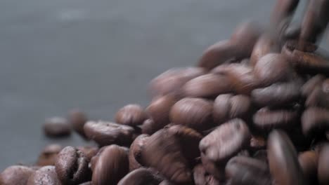 Slow-motion-footage-of-roasted-Ecuadorian-coffee-beans-falling-onto-a-gray-table,-a-mesmerizing-visual-delight