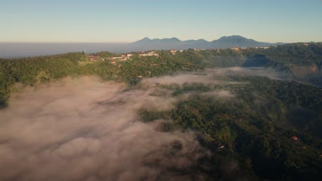 Aerial-view-rising-over-a-misty-valley,-toward-Kintamani-town,-sunrise-in-Bali