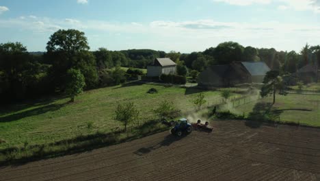 Cinematic-aerial-shot-of-tractor-in-France-landscape,-trees,-roads-and-villages