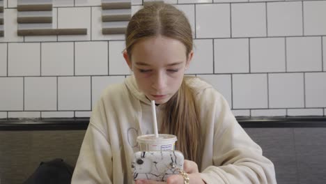 Teenager-Mädchen-Im-Fast-Food-Restaurant-Trinkt-Und-Schaut-Auf-Ihr-Smartphone