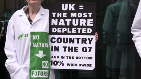 Un-Científico-Con-Una-Bata-Blanca-Sostiene-Un-Cartel-Que-Dice:-“Reino-Unido-=-El-País-Con-Mayor-Degradación-De-La-Naturaleza-En-El-G7-Y-En-El-10%-Inferior-Del-Mundo”.