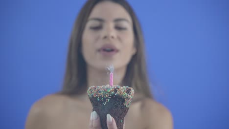 Eine-Schöne-Junge-Frau-Bläst-Eine-Geburtstagskerze-Auf-Einem-Cupcake-Aus