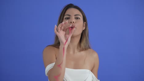 Beautiful-girl-blows-a-red-party-streamer-at-camera,-isolated-on-blue-background