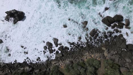 Top-down-view-of-rocky-coastline-with-powerful-sea-waves-leading-up-to-it