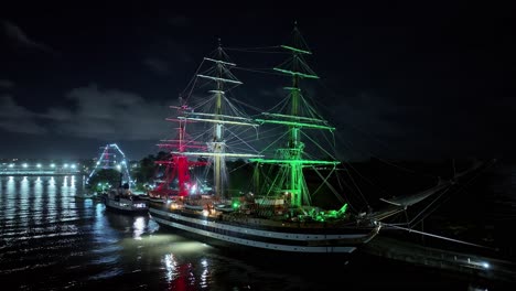 Drone-shot-showing-Amerigo-Vespucci-Navy-ship-lighting-in-red-white-green-colors-at-night---docking-at-harbor-of-Dominican-Republic