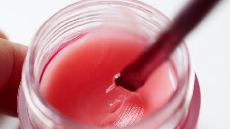 Blending-a-moist-pink-lip-gloss-with-a-small-applicator-in-a-container,-in-preparation-for-a-full-make-up-application