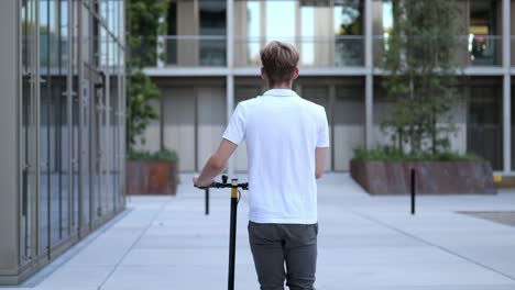 Back-view-of-a-young-businessman-walking-with-an-e-scooter-medium-shot