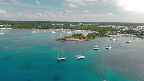 Drone-flying-over-luxury-boats-moored-in-tropical-waters-of-Bayahibe-tourist-port,-La-Romana-in-Dominican-Republic