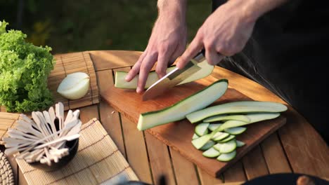 High-angle-view-of-a-male-cutting-zucchini-into-long-slices-in-his-garden