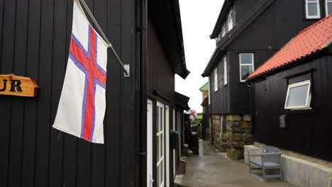 Gentle-breeze-blowing-on-Faroese-flag-on-wooden-exterior-in-Gasadalur,-Vagar,-Faroe-Islands
