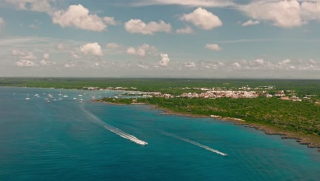 Drone-flying-over-blue-sea-of-Bayahibe-coast,-Dominican-landscape,-La-Romana