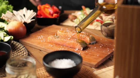 A-young-man-pours-oil-over-a-piece-of-salmon-surrounded-by-vegetables
