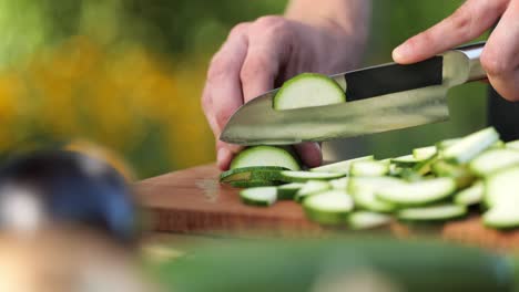 Young-man-cutting-zucchini-on-a-wooden-board-in-his-garden-close-up