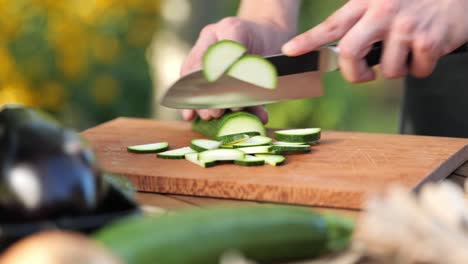 Young-man-cutting-zucchini-on-a-wooden-board-in-his-garden-close-up