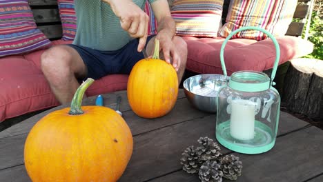 Young-dad-carves-pumpkin-on-garden-terrace,-sunny-autumn-day