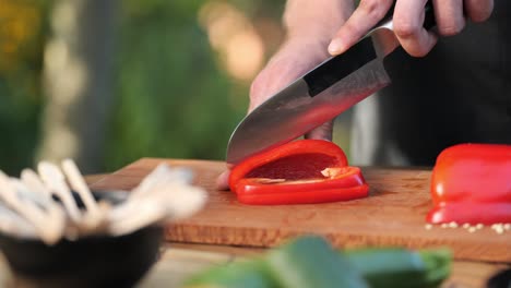 Young-man-cutting-peppers-on-a-wooden-board-in-his-garden-close-up