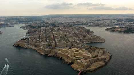 Aerial-tilt-shot-in-front-of-the-Fort-Saint-Elmo-and-the-Valletta-cityscape,-sunset-in-Malta