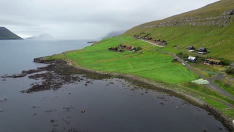 Drone-flying-backwards-reveals-a-green-Faroese-and-cloudy-landscape-with-turf-roof-houses-in-Kirkjubour
