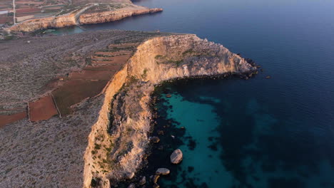 Aerial-view-tilting-over-the-rocky-coastline-of-the-Malta-island,-during-sunset