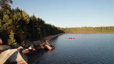 High-aerial-of-red-canoe-on-pristine-wilderness-lake-at-golden-hour