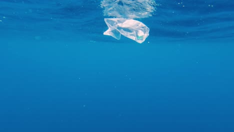 floating-plastic-waste-at-the-surface-of-water,-underwater-slow-motion