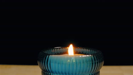 Small-Candle-in-Glass-Container-Blown-Multiple-Times-and-Finally-Extinguished-Against-a-Black-Backdrop