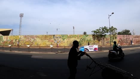 Hombre-Empujando-El-Carro-En-La-Calle-Con-Mural-De-Graffiti-En-El-Fondo-En-Dakar,-Senegal