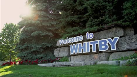 Beschilderung-„Willkommen-In-Whitby“-In-Kanada-Mit-Wärmendem-Licht,-Das-Durch-Die-Bäume-Strahlt,-Mit-Einem-Schwenk-Aus-Niedrigem-Winkel