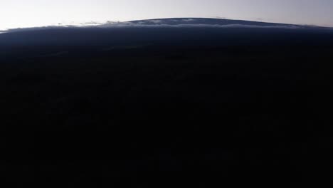 Aerial-close-up-tilting-up-shot-of-Mauna-Loa-peeking-above-the-clouds-at-sunset-on-the-island-of-Hawai'i