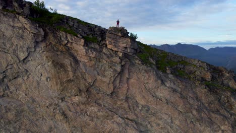 Hiker-standing-on-the-edge-of-a-steep-cliff-during-summer-on-the-hiking-trail-to-Hesten,-Senja-Island