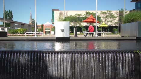 Sidetracking-Shot-of-a-Waterfall-Over-a-Wall-at-Whitby-Public-Library-Square-with-Modern-Architecture-in-the-Background