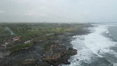 Aerial:-Tourists-explore-low-tide-rocks-at-Tanah-Lot-Temple-on-Bali