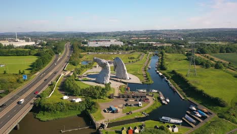 Aerial-Shot-Flying-Behind-The-Kelpies,-A-Scottish-Landmark-of-Horses-in-Falkirk-Next-to-a-Canal-on-a-Sunny-Day-in-Summer