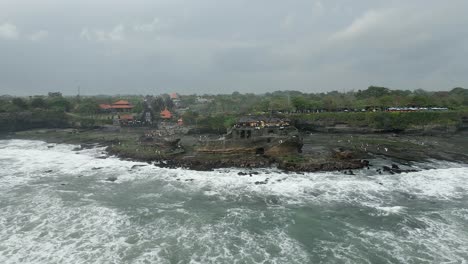 Aerial-retreats-from-coastal-Bali-rock-formation,-Tanah-Lot-Temple