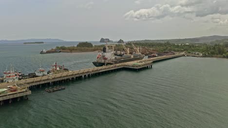 Push-in-view-of-freighters-and-barges-being-loaded-with-nickel-rich-ore-at-a-Sumimoto-mining-site-in-Taganito,-Philippines