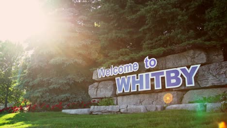 "Welcome-to-Whitby"-is-prominently-displayed-on-a-sign-affixed-to-a-stone-wall-beneath-a-canopy-of-trees,-as-the-camera-smoothly-pans-to-capture-the-scene