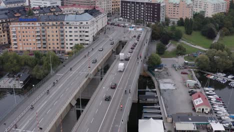 Drone-shot-orbiting-and-panning-down-on-traffic-and-bikers-passing-on-Liljeholmsbron-towards-Hornstull,-Söder,-Stockholm