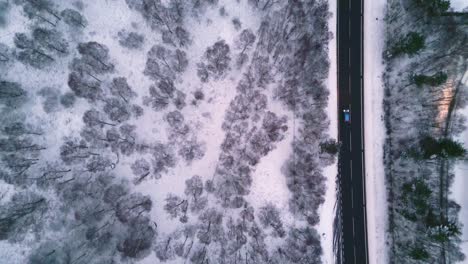 Top-down-panning-shot-of-cars-driving-on-road-in-winter-landscape