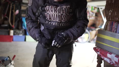 Harley-Davidson-Biker-Zieht-In-Seiner-Garage-Schutzhandschuhe-An-Und-Schließt-Die-Jacke