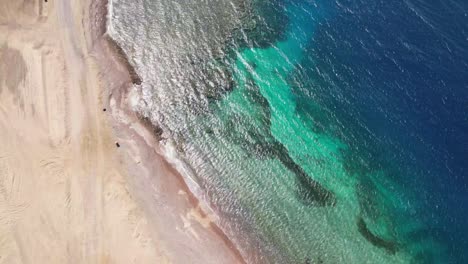 Aerial-birdseye-descending-over-deserted-beach-with-turquoise-waters,-Tabuk