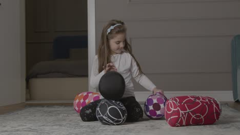 Young-Girl-Trying-To-Stack-Round-Cushions-On-Floor-Before-They-Fall-Over