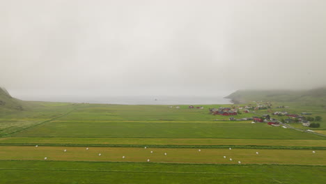 Vista-Aérea-De-La-Pradera-Verde-En-El-Pueblo-De-Unstad-En-Una-Mañana-Brumosa-En-La-Isla-Vestvagoya,-Noruega