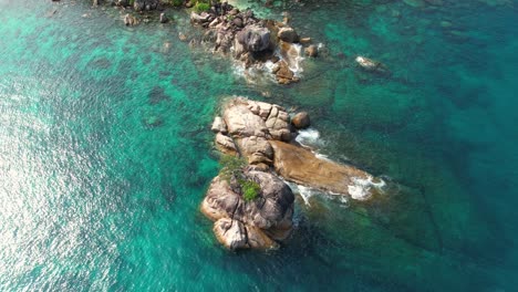 slow-motion-bird-eye-drone-shot-over-granite-rock-at-sea-on-mahe-island,-waves-and-turquoise-water,-Seychelles-1