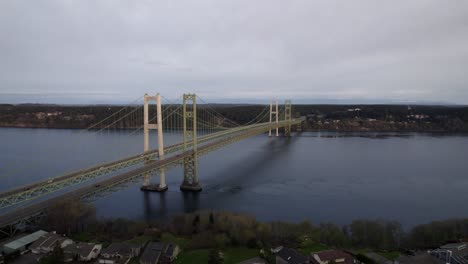 Light-traffic-flowing-along-the-Tacoma-Narrows-Bridge,-dull-cloudy-skies,-aerial-wide-angle