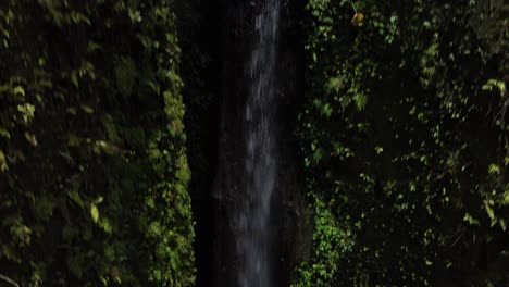 Rainbow-flare-on-pouring-waterfall,-pull-up-shot-reveal-village,-Bali