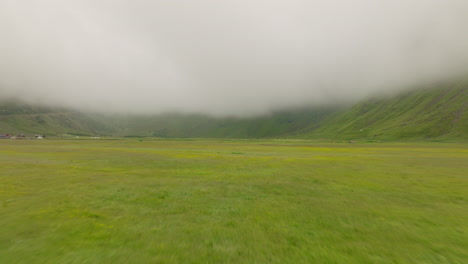 Flying-Over-The-Green-Grassland-Towards-The-Mountain-Covered-By-Fog-And-Clouds-In-Norway