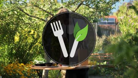 Digital-symbol-Fork-and-leaf-knife-for-conscious-vegan-diet-in-front-of-cooking-area-with-male-chef-in-outdoor-kitchen-on-sunny-day