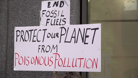 In-slow-motion-a-handmade-cardboard-protest-placard-is-held-up-that-reads,-“End-fossil-fuels,-protect-our-planet-from-poisonous-pollution”