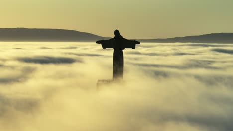 Sunrise-above-the-clouds,-with-birds-crossing-the-horizon-by-the-statue-and-the-fog-moving