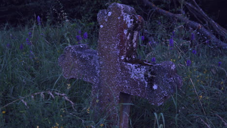 Old-cross-on-the-grave-of-an-unknown-person-amidst-the-grass-and-flowers-at-the-edge-of-the-forest,-evening-scene